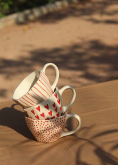 three coffee cups stacked on top of each other with hearts painted on them, sitting on a table