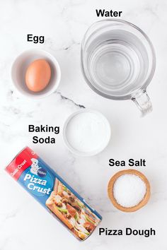 ingredients needed to make pizza dough laid out on a white marble counter top, including eggs, water, baking soda, sea salt, and pizza dough