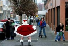 a man dressed as santa claus riding a bike down the street with people standing around