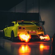 two yellow cars with red flames on them in a dark room, one has its lights on and the other is off