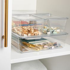 three clear containers with gold handles on top of a white shelf filled with office supplies