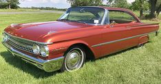 an old red car is parked in the grass