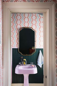 a pink sink sitting under a mirror in a bathroom next to a wallpapered wall