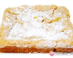 a square piece of cake with powdered sugar on top, sitting on a white surface