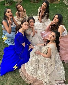 several women are sitting on the grass posing for a photo with their fingers in their mouths