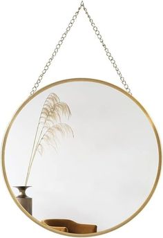 a round mirror hanging on a chain with a plant in the center and a vase behind it