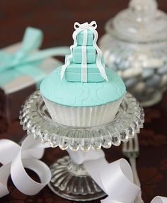 there is a cupcake with a bow on it sitting on a glass stand next to some white ribbons