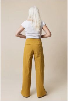 the back view of a woman wearing mustard colored pants and white t - shirt, with her hands on her hips