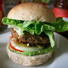 a hamburger with lettuce, tomato and cucumber on it sitting on a white plate