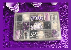 a plastic box filled with purple and white candies on top of a purple sequin floor