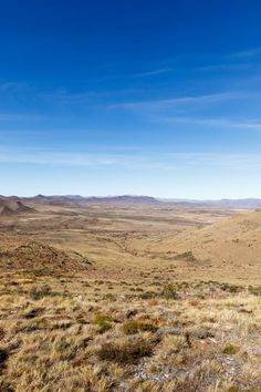 an open field with mountains in the distance and blue skies above it on a sunny day