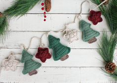 crocheted christmas ornaments hanging from pine needles on a white wooden background with pine cones