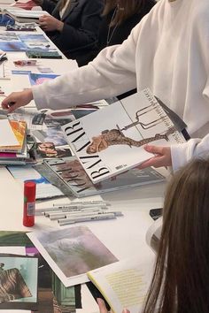 several people sitting at a table with books and magazines on it, one person is pointing to the book