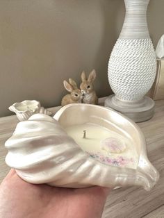 a hand holding a candle in front of a white vase with two rabbits on it