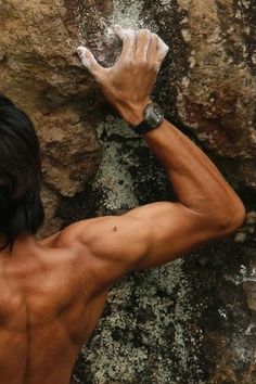 a shirtless man climbing up the side of a rock