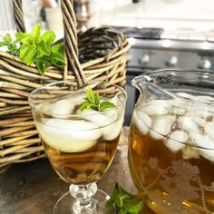 two glasses filled with liquid and ice sitting on a counter next to a wicker basket