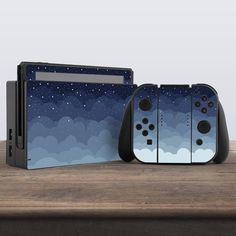 two video game controllers sitting next to each other on top of a wooden table with clouds and stars in the sky