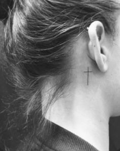 a woman's neck with a small cross tattoo on the back of her left ear