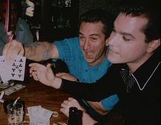 two men sitting at a table with cards in front of them and one man pointing