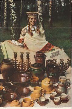 there is a woman sitting in the woods surrounded by teapots and other items