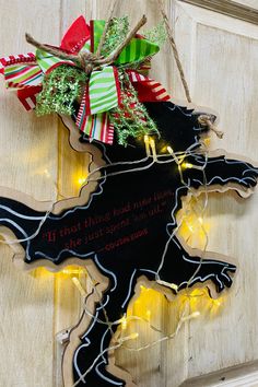 a christmas decoration hanging from the side of a wooden door with lights and ribbon around it