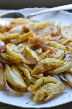 a white plate topped with onions on top of a wooden table next to a knife and fork