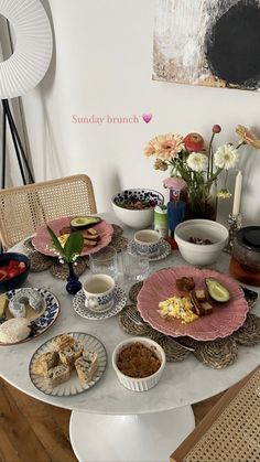 a table with plates and bowls of food on it in front of a vase filled with flowers