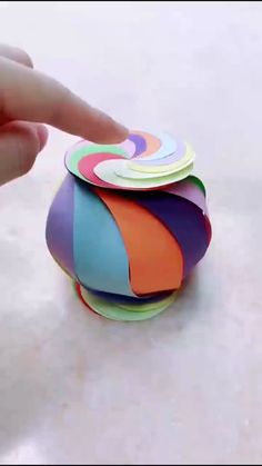 a hand is touching the top of a stack of colorful coasters on a white surface