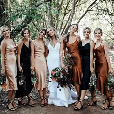 a group of women standing next to each other in front of trees and bushes wearing dresses