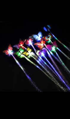 several colorful lights in the shape of butterfly wands on a black background with one glowing