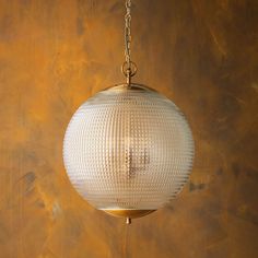 a glass ball hanging from a chain in front of a gold wallpapered background