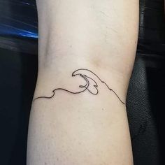 a hand holding a wave tattoo on the left side of the arm with black ink