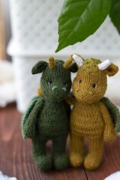 two knitted animals sitting next to each other on a wooden floor with a plant in the background