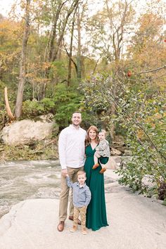 a man and woman pose with their son in front of a river surrounded by trees