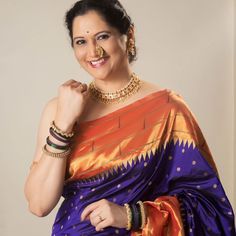 a woman in an orange and blue sari with gold jewelry on her neck smiling