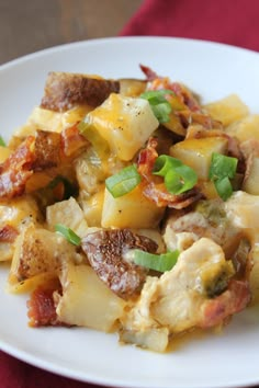 a white plate topped with potatoes and meat covered in cheese, green onions and seasoning