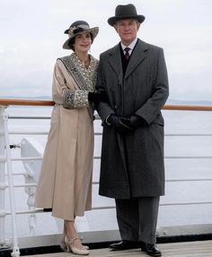 an older man and woman standing next to each other on a deck near the ocean