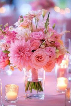 a vase filled with lots of pink flowers on top of a table next to candles