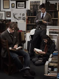 three people sitting in chairs reading books and looking at something on the floor next to them