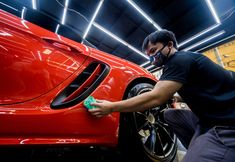 a man polishing a red sports car in a garage while wearing a face mask