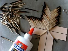 some matches are laying on the floor next to a bottle of glue and sticks that have been cut out