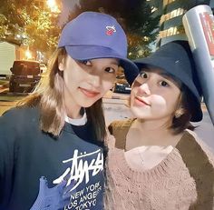 two young women standing next to each other in front of a parking meter on a city street