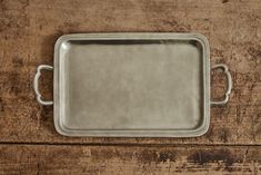 an empty metal tray sitting on top of a wooden table next to a knife and fork