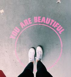 two people standing in front of a sign that says you are beautiful on the ground