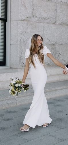 a bride and groom walking down the street holding hands