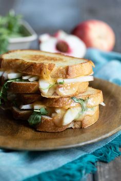 a grilled cheese sandwich is stacked on a plate with fresh herbs and apples in the background