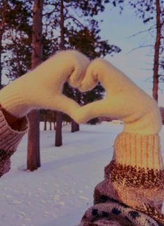 two hands in mittens making a heart shape with their fingers on snow covered ground