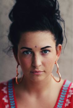 a woman with large hoop earrings and piercings on her face looking at the camera