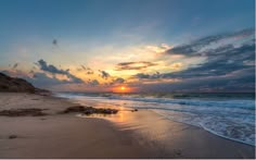 the sun is setting at the beach with waves coming in to shore and sand on the ground