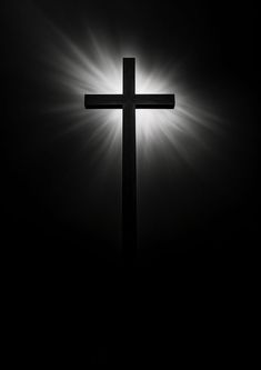 a black and white photo of a cross with the sun shining through it's shadow